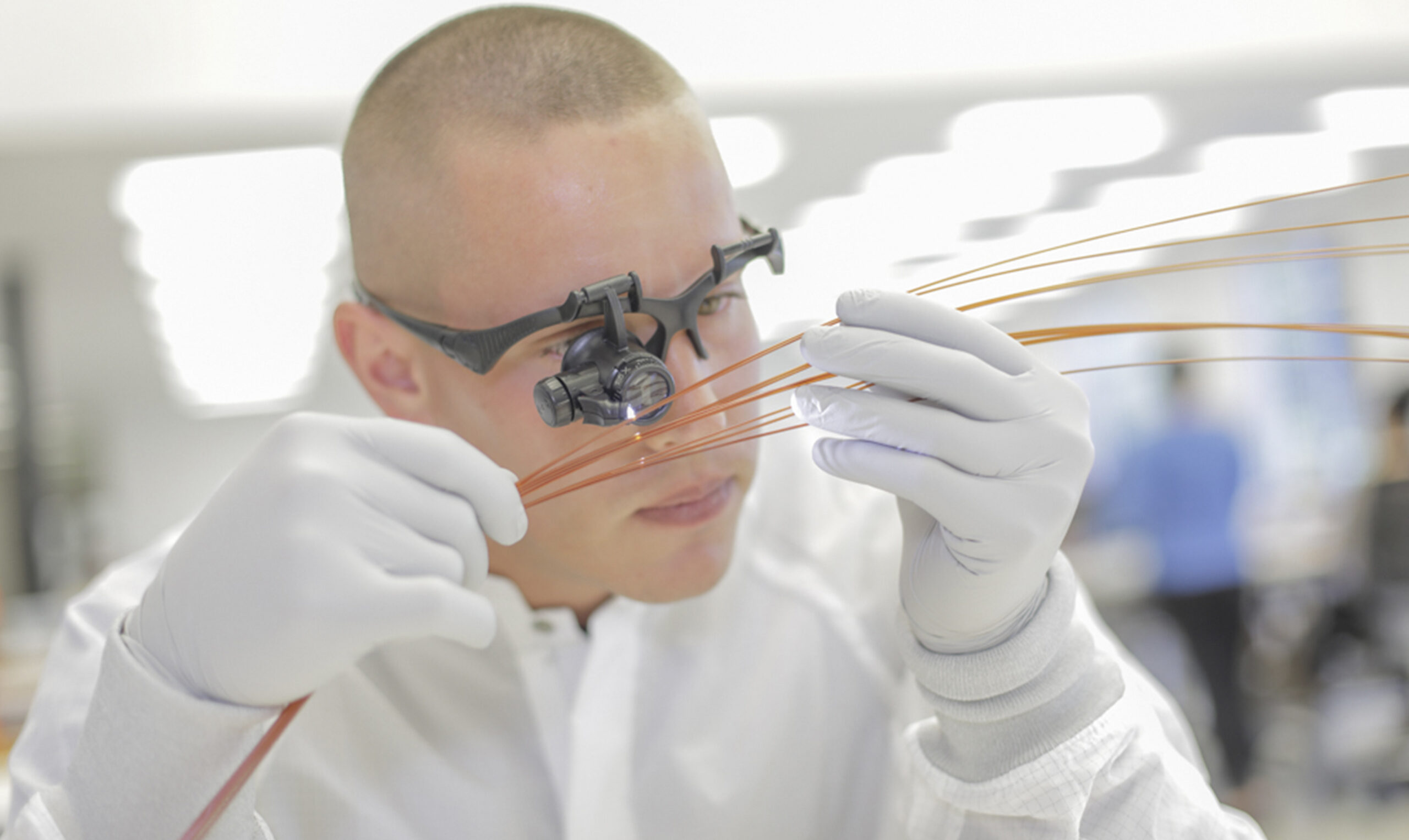 A technician examines fiber optic cables with magnifying glasses, wearing gloves and a lab coat, showcasing precision in telecommunications work.
