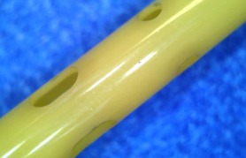 Close-up of a yellow musical flute showcasing several finger holes along its length. The vibrant background enhances the flute's details.