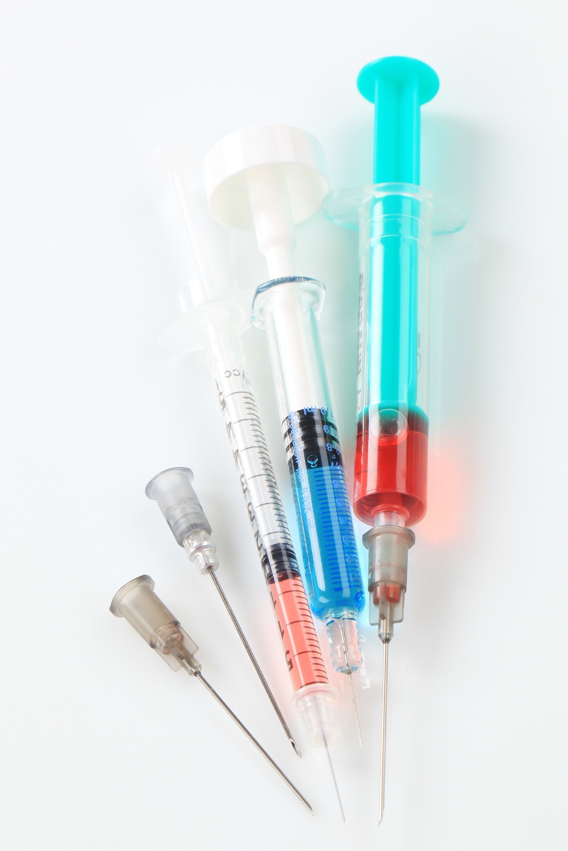 Assorted syringes and needles filled with colored liquids, illustrating medical supplies used for vaccinations or injections.