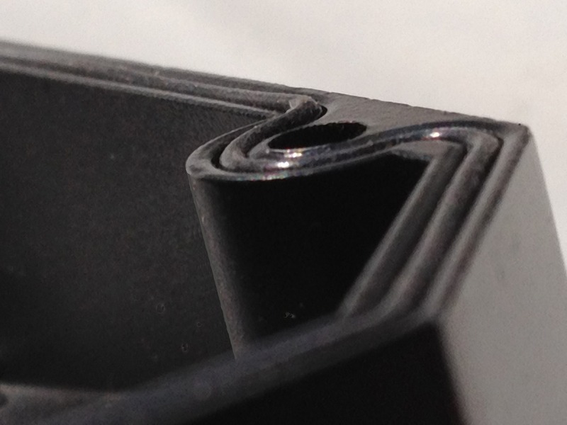 Close-up of a black, textured corner of a rolled edge, highlighting the smooth curve and sharp line quality, emphasizing material design and craftsmanship.